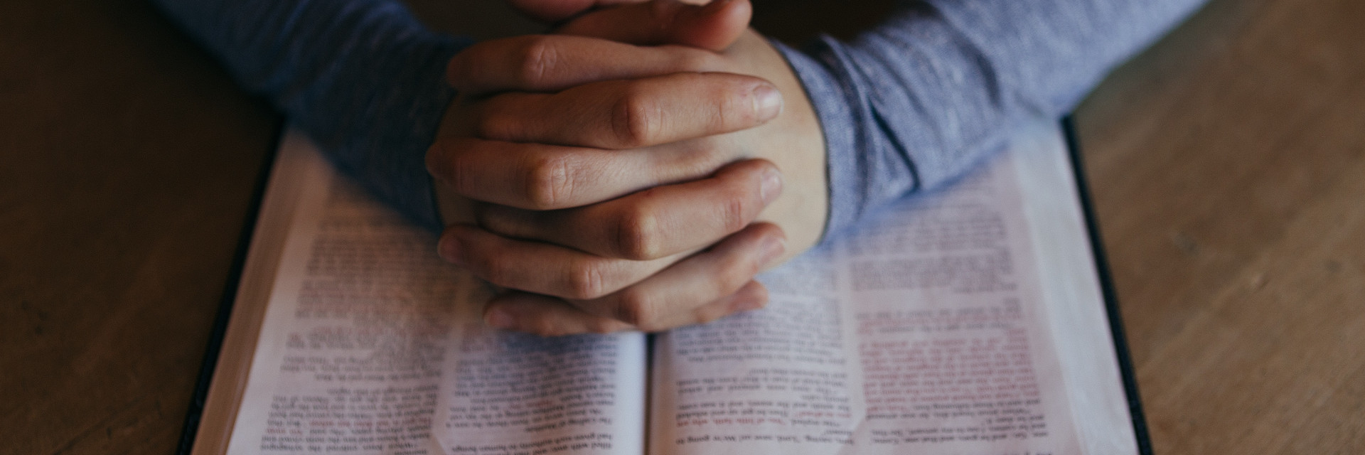 Folded hands lay on an open Bible